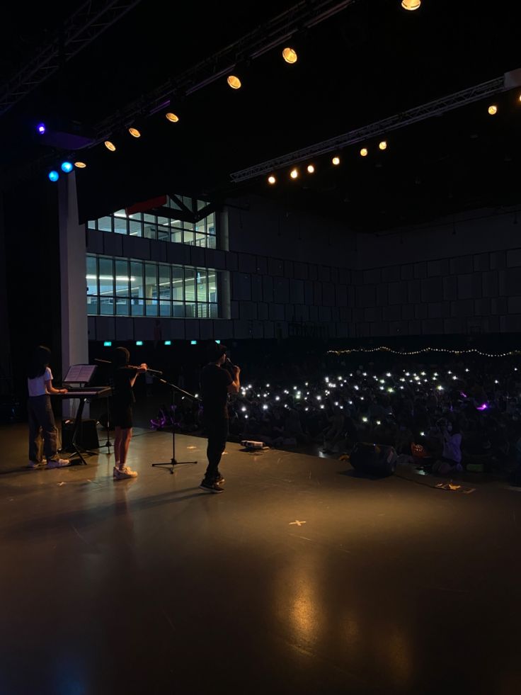 two people are standing on stage with microphones in front of an audience at night