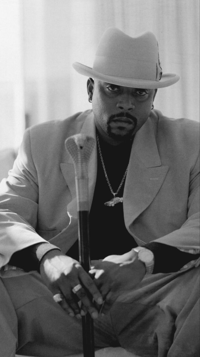 a man in a suit and hat sitting on a couch with his hands folded out