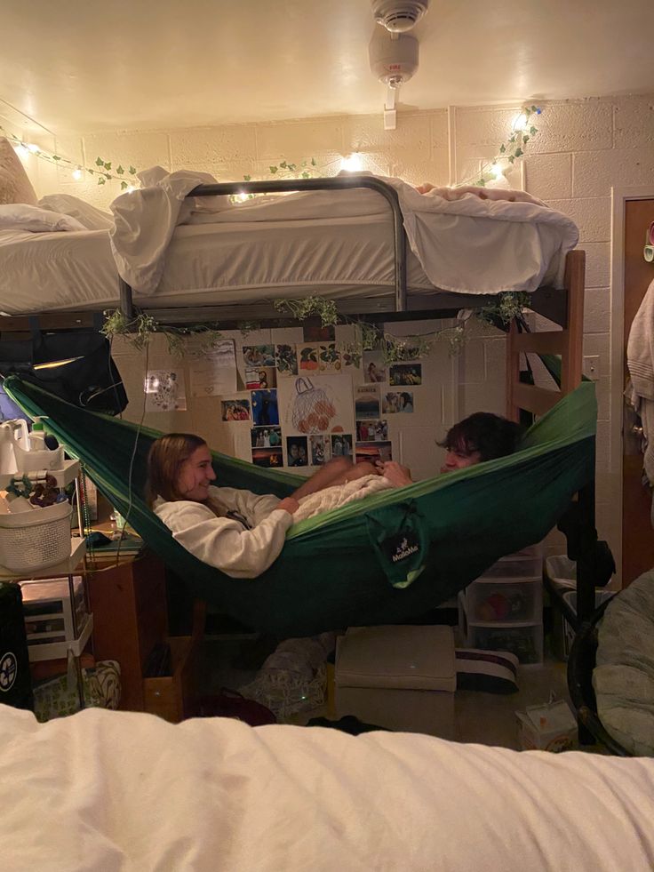 two people sitting in a hammock with lights strung over the top bunk beds