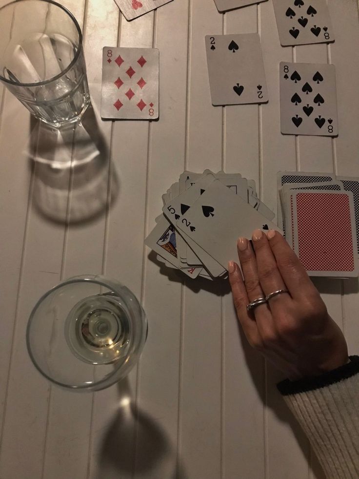 a table with playing cards, wine glass and two people holding their hands over them