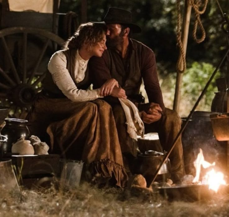 a man and woman sitting next to each other in front of a tent with fire