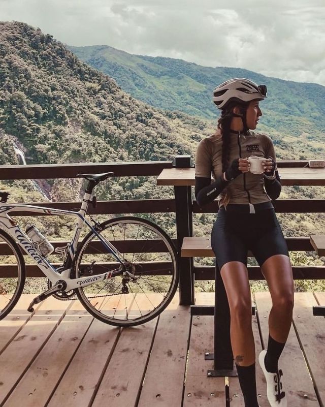 a woman sitting on top of a wooden bench next to a bike near a mountain