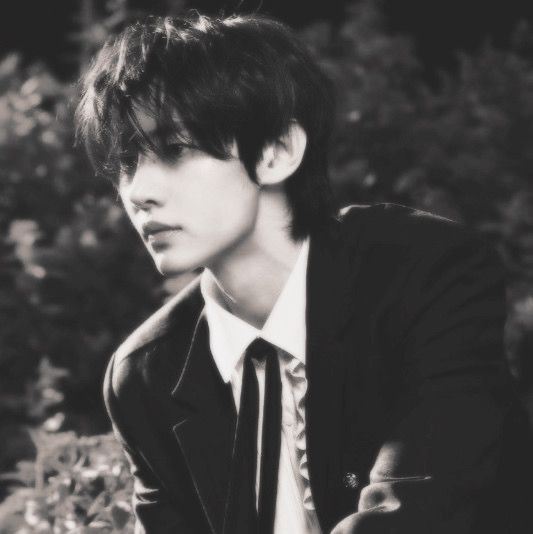 black and white photograph of a young man wearing a suit and tie with bushes in the background