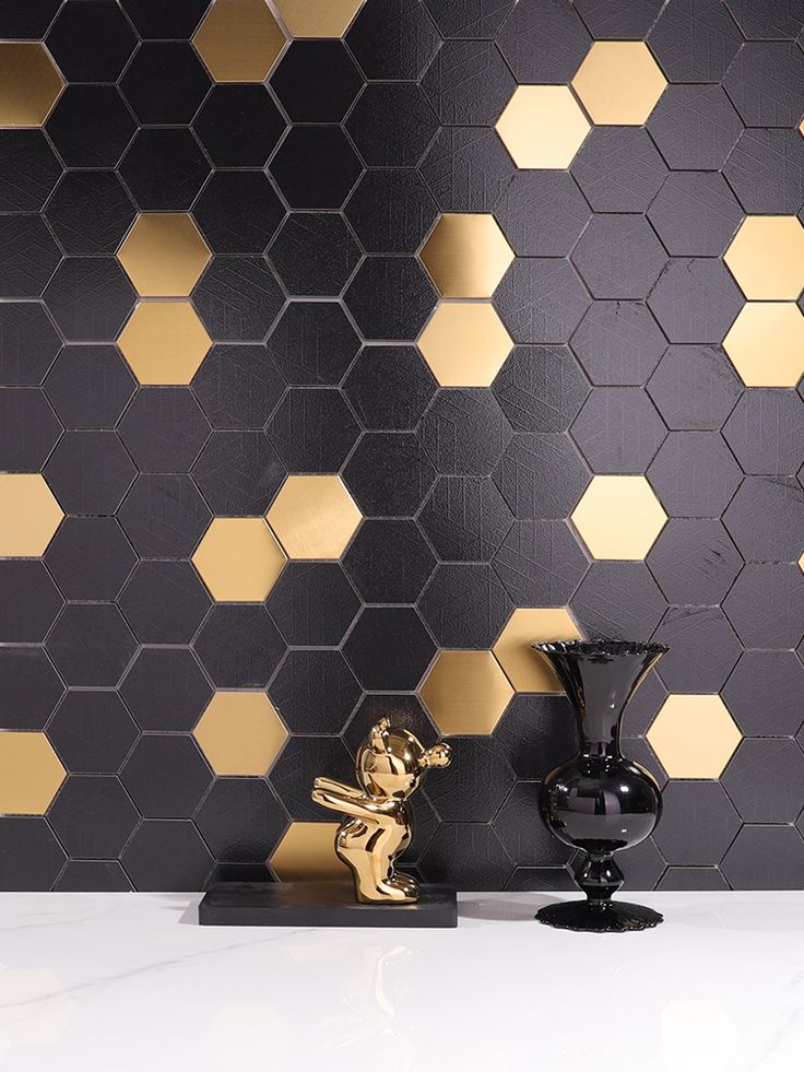 a black vase sitting on top of a white counter next to a wall covered in gold hexagonal tiles