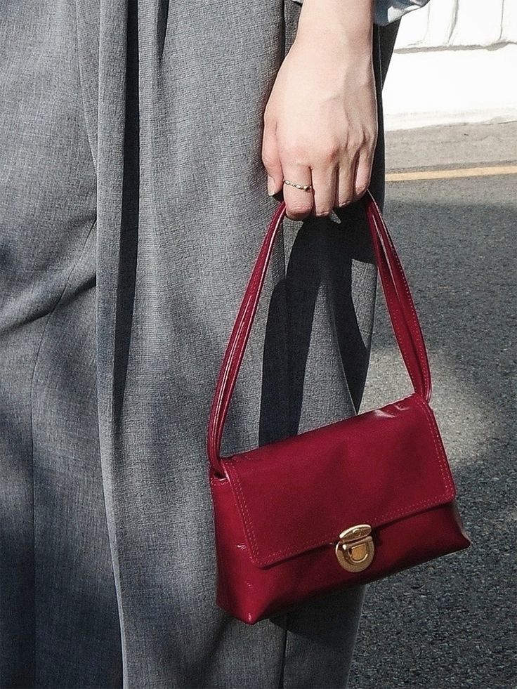 a woman is holding a red purse on the street