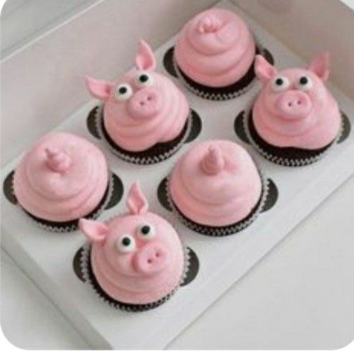 four cupcakes with pink frosting and pig faces on them in a box