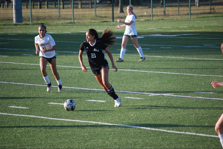 girls playing soccer on a field with one girl running after the ball while another runs towards her