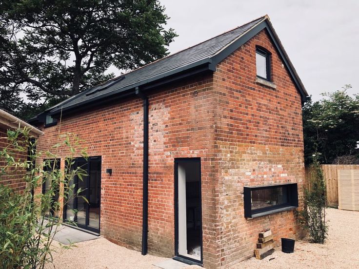 a small brick building with a black door and window on the outside, next to a tree