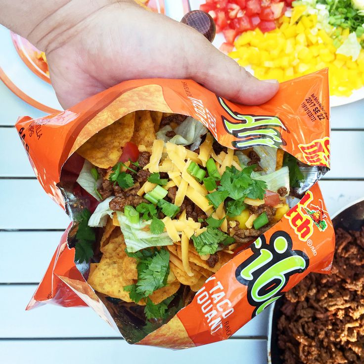 a hand holding a bag of nachos next to a bowl of salad