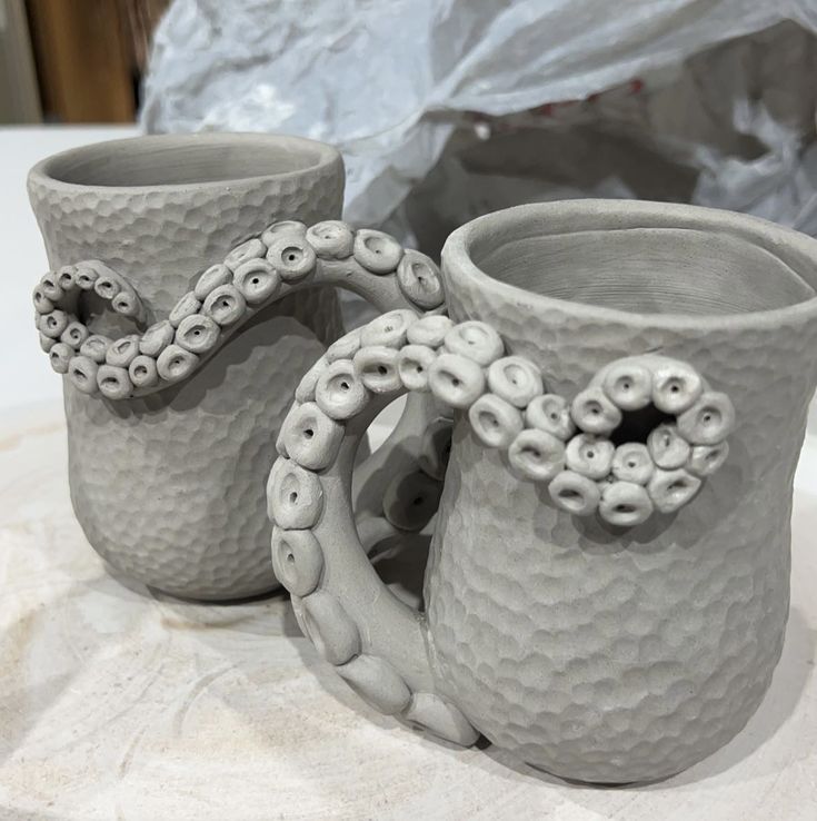 two white vases sitting next to each other on top of a cloth covered table