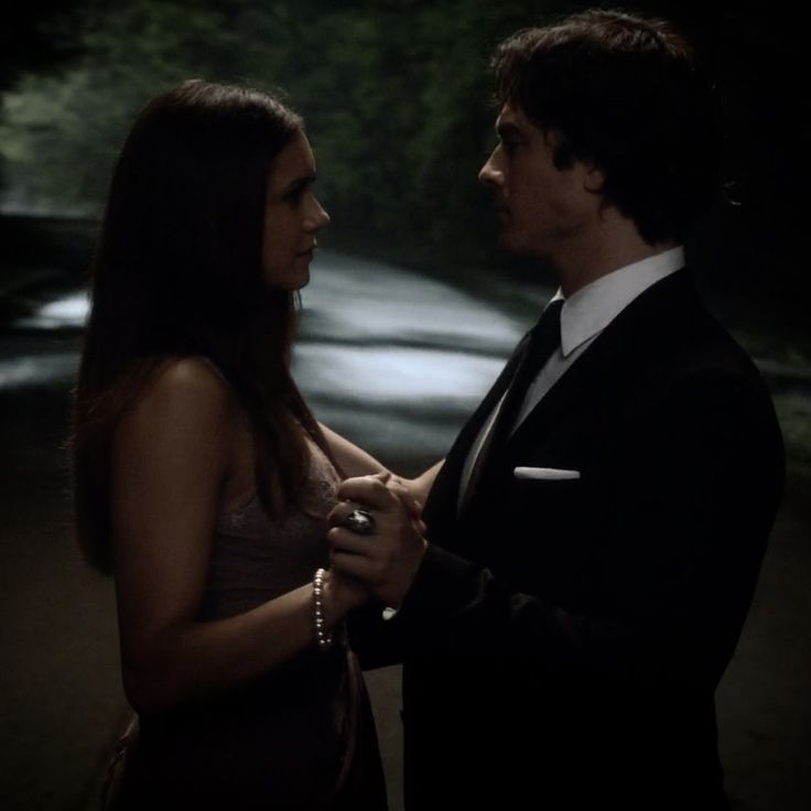 a man in a tuxedo standing next to a woman wearing a beaded necklace