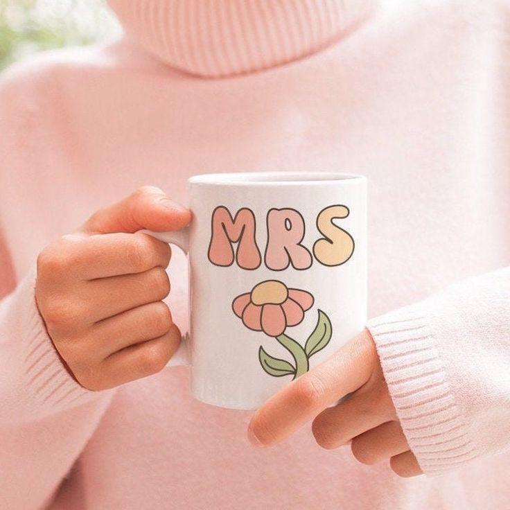 a person holding a coffee mug with the word mrs on it and flowers painted on it