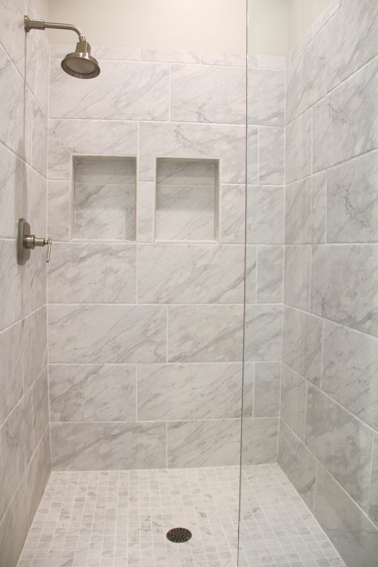 a walk in shower sitting next to a white tiled wall and floor with two niches on each side