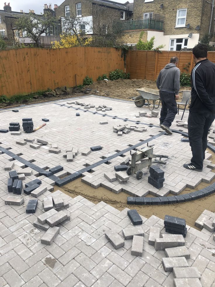 two men are standing in the middle of a yard that is being built with bricks