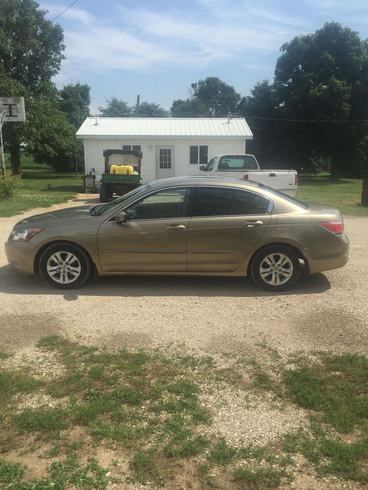 a brown car parked in front of a house on a gravel lot next to grass and trees