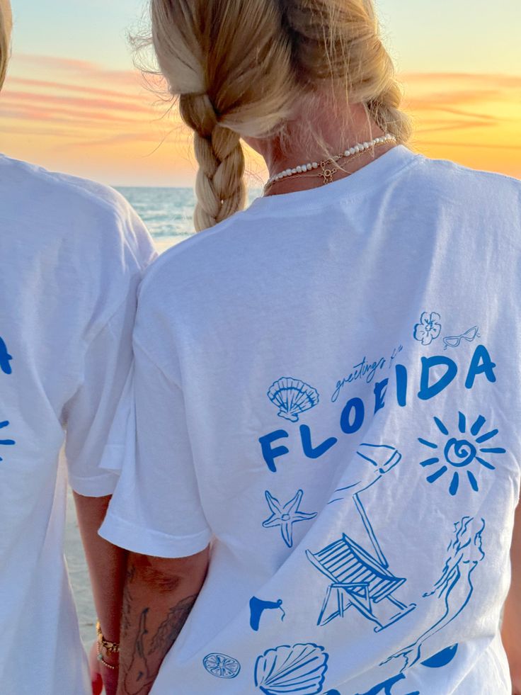 Our EXCLUSIVE Greetings From Florida Sunhoney T-shirt is perfect for beach lovers! This Comfort Colors t-shirt features a playful blue drawn design of popular Florida symbols like the sun, shell, mermaid, and more. Style this shirt over your fave bikini as your new go-to beach tee or style with biker shorts and sneakers for the cutest summer fit! Designed by us, handmade by us in Jacksonville Beach, FL Product is made to order: available for pick up/ships in 2-4 business days Content: 100% Cotto Graphic Tee T-shirt For Family Vacation, Cute Tees For Women, Relaxed Fit T-shirt For Family Beach Vacation, Fun Custom Print Tops For Beach Season, Blue Top With Custom Print For Summer, Blue Tops With Custom Print For Summer, Casual Blue Tops For Family Vacation, Blue T-shirt With Custom Print For Summer, Graphic Print T-shirt For Family Vacation, Relaxed Fit