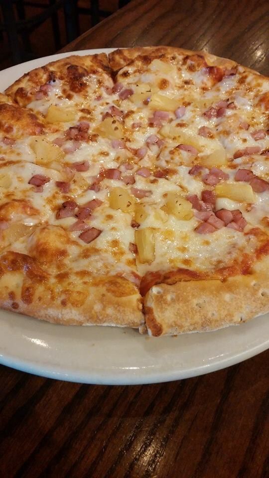 a pizza with pineapple and ham on a white plate sitting on a wooden table