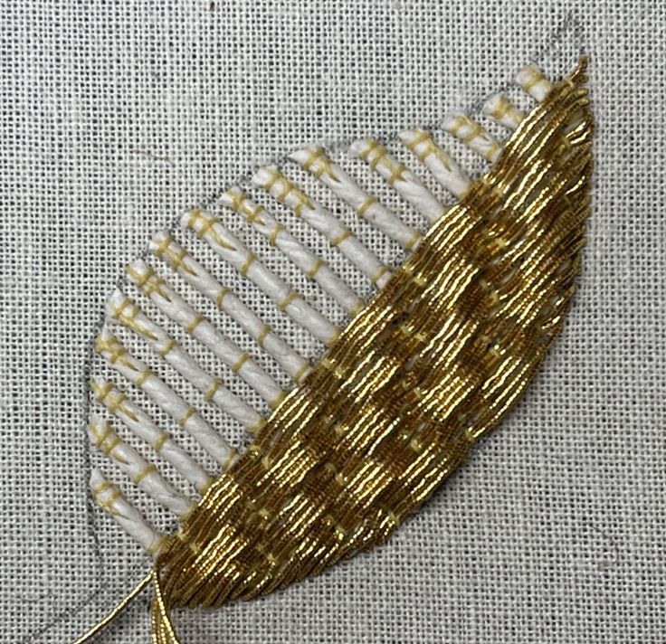 a gold and white piece of fabric with some thread on it's side, in the shape of a leaf