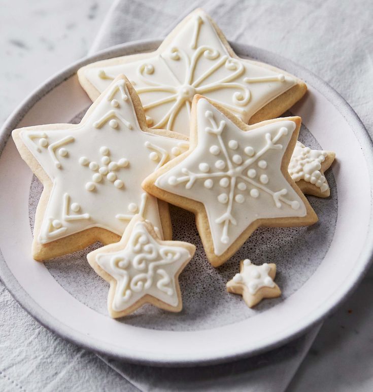 some cookies are on a plate and one is decorated with white icing, the other has snowflakes