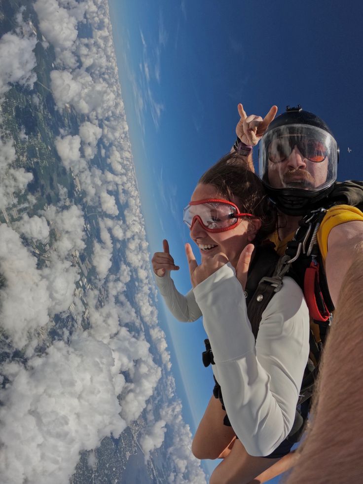 two people are flying in the sky with their hands up and one person is wearing goggles