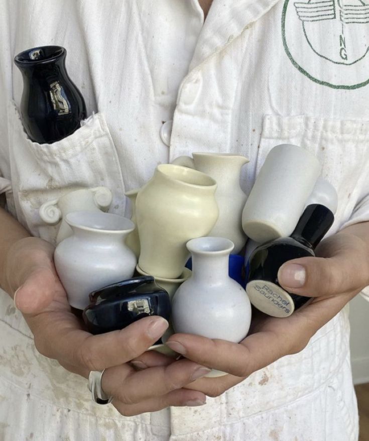 a person holding several different sized vases in their hands, all white and black