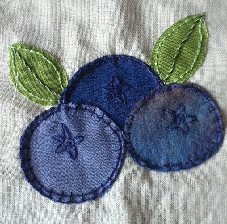 three blue and green appliques are on a white fabric material with stitching