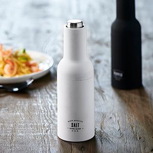 a white bottle sitting on top of a wooden table next to a plate of food