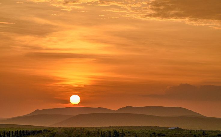 the sun is setting over some hills