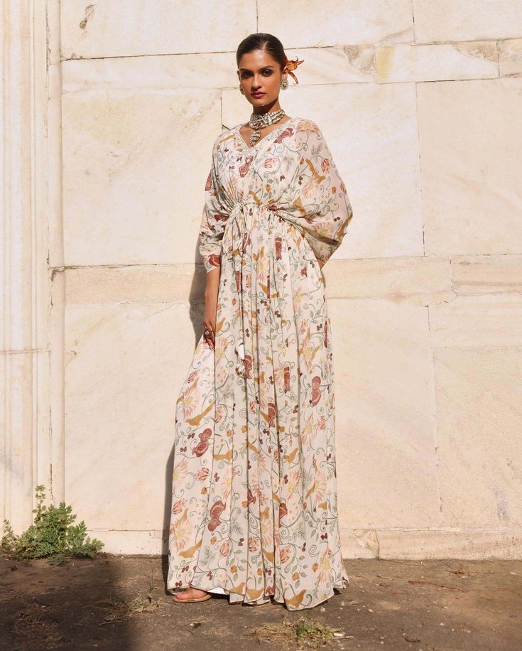 Introducing this mesmerizing printed full-length draped kaftan, where vibrant prints meet elegant detailing with an embellished neckline. This kaftan is the epitome of effortless style, offering both comfort and sophistication. Perfect for leisurely days or glamorous evenings, its flowing silhouette and intricate embellishments ensure you stand out with grace. Embrace luxury and make a statement with this exquisite kaftan that's sure to elevate your look wherever you go. Festive Printed Dress With Kimono Sleeves, Festive Printed Dresses With Kimono Sleeves, Bohemian Wedding Dress With Digital Print, Elegant Floral Print Tunic Kaftan, Elegant Tunic Dress With Printed Motifs, Elegant Floral Print Festive Kaftan, White Maxi Dress With Draped Sleeves, Maxi Length Kalamkari Print Dress For Eid, Eid Digital Print Maxi Length Kurta