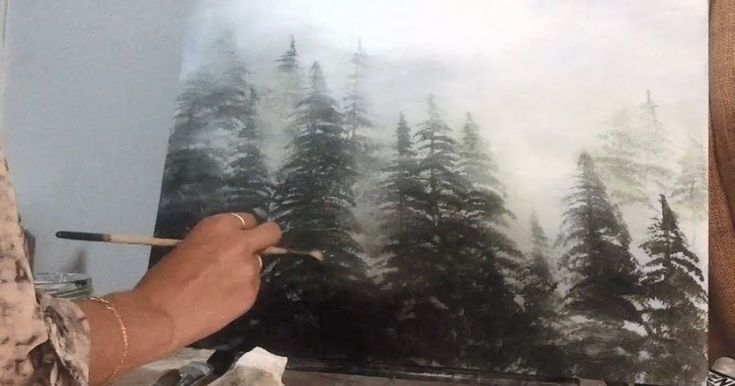 a man is painting a forest scene with trees in the background and fog on the ground