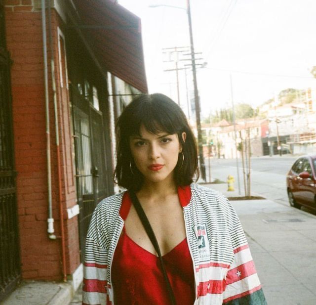 a woman standing on the side of a street next to a red brick building wearing a striped cardigan