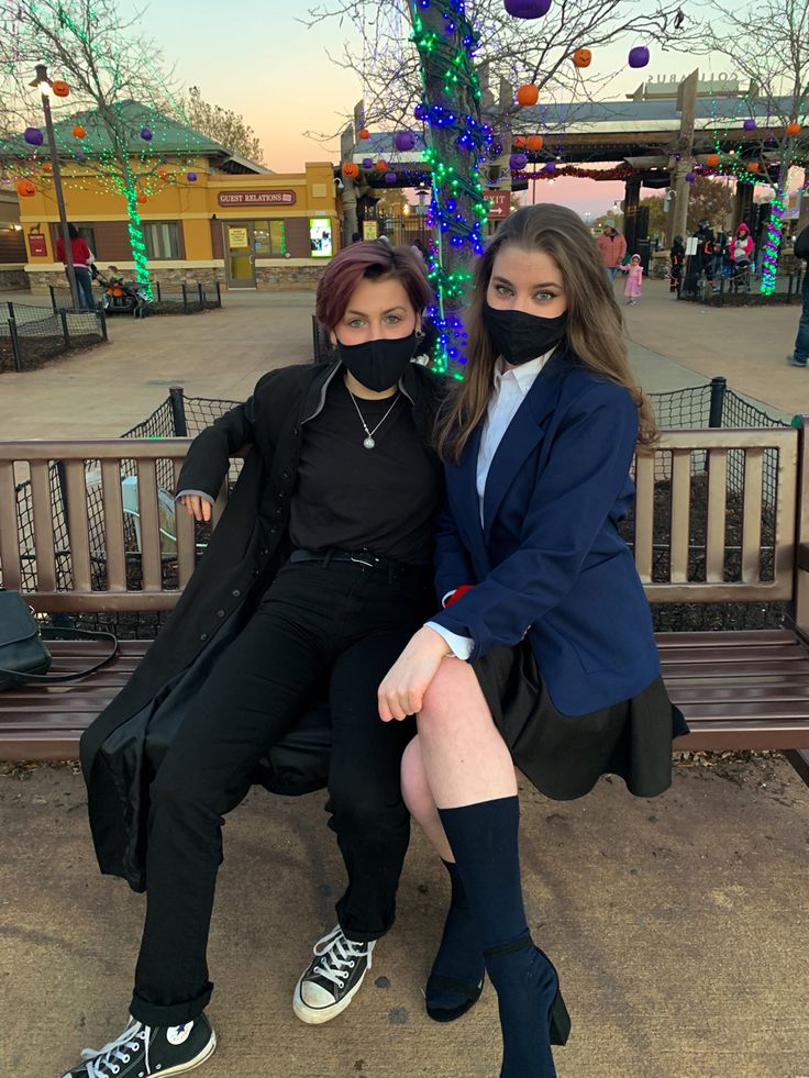 two young women sitting on a bench wearing face coverings and black pants, one with her legs crossed