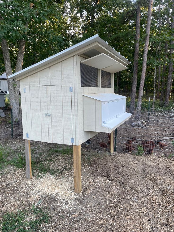 a chicken coop built into the side of a fenced in area next to trees