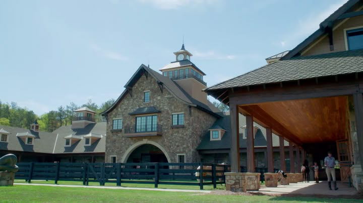 a large stone building with a black fence and people standing in the front yard looking at it