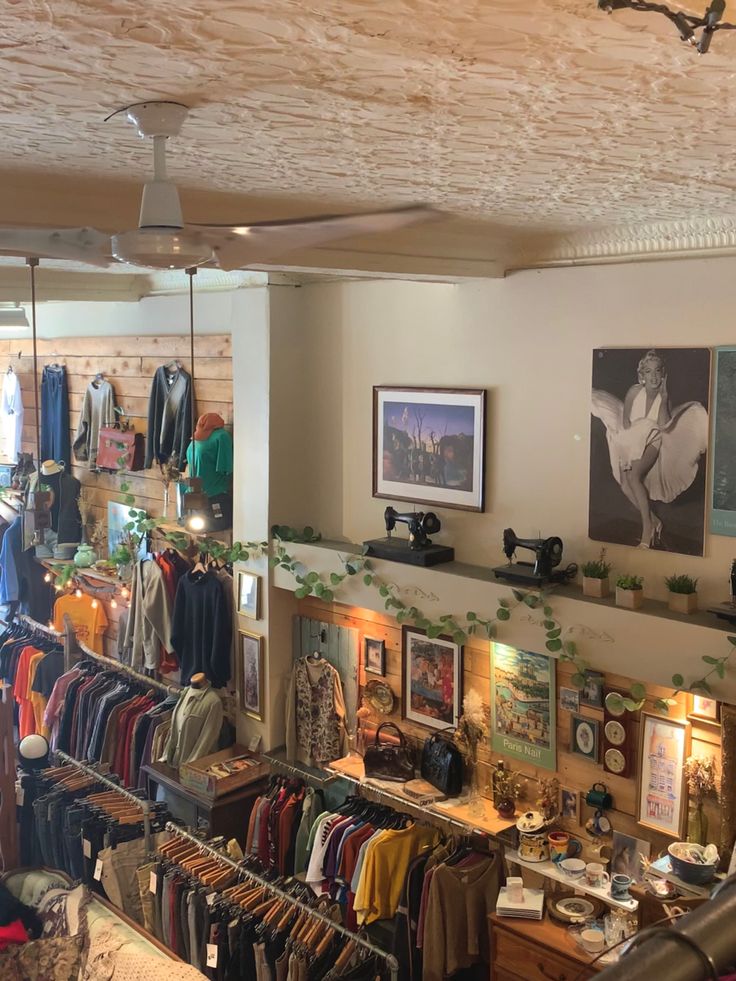 the inside of a clothing store with lots of clothes on racks and pictures hanging from the ceiling