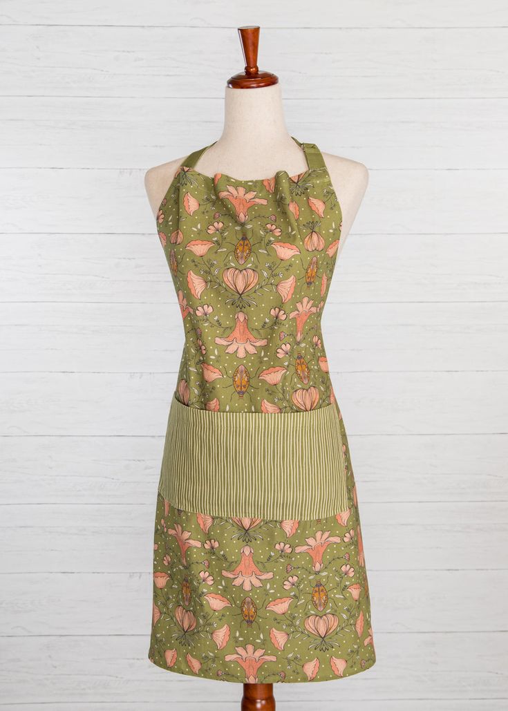 an apron on a mannequin wearing a green dress with pink and orange flowers