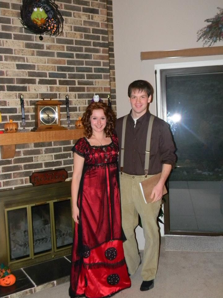 a man standing next to a woman wearing a red dress in front of a brick wall