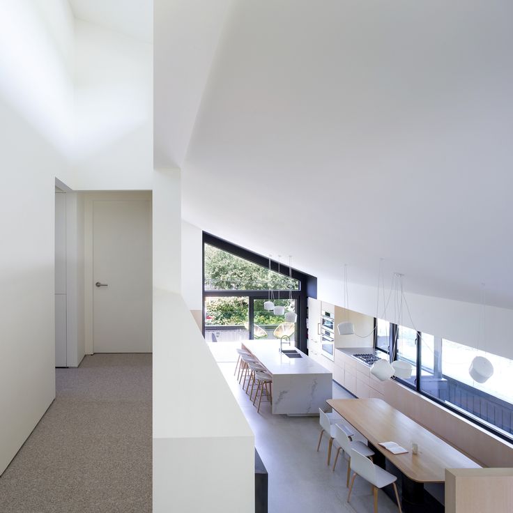 an open kitchen and dining room area in a modern house with white walls, floor to ceiling windows, and large sliding glass doors