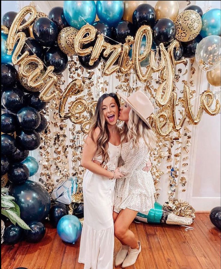 two women standing next to each other in front of balloons