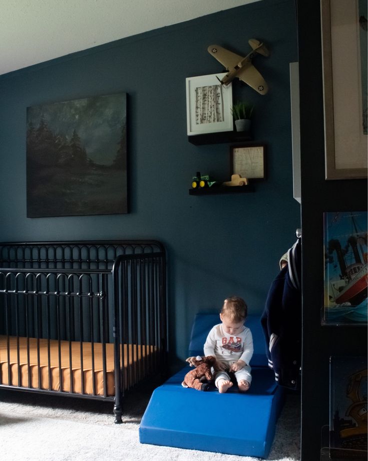 a baby sitting on top of a blue mattress in a room with a crib