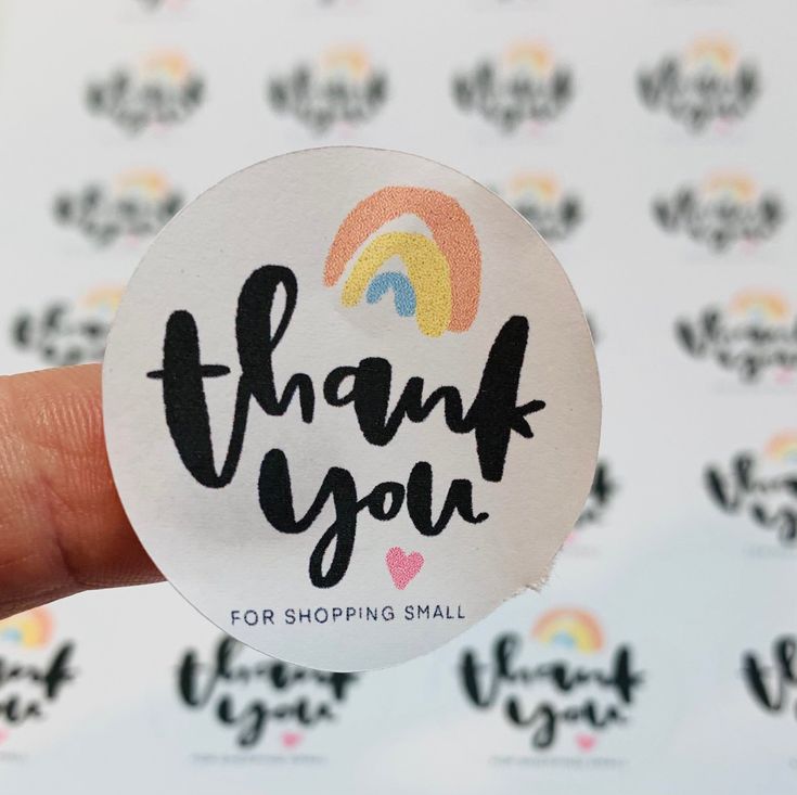 a hand holding up a sticker with the words thank you for shopping small on it