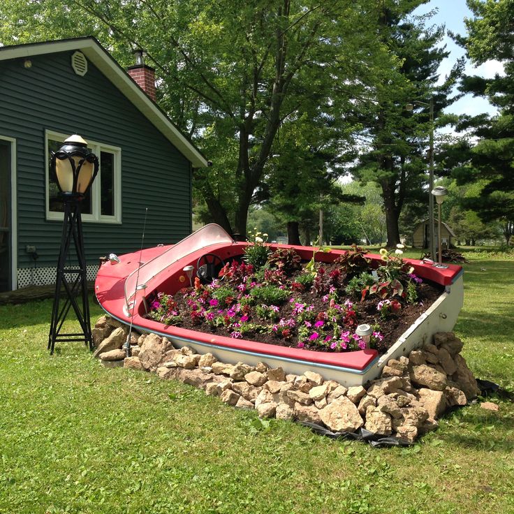 a boat shaped planter filled with flowers in front of a green house on the grass