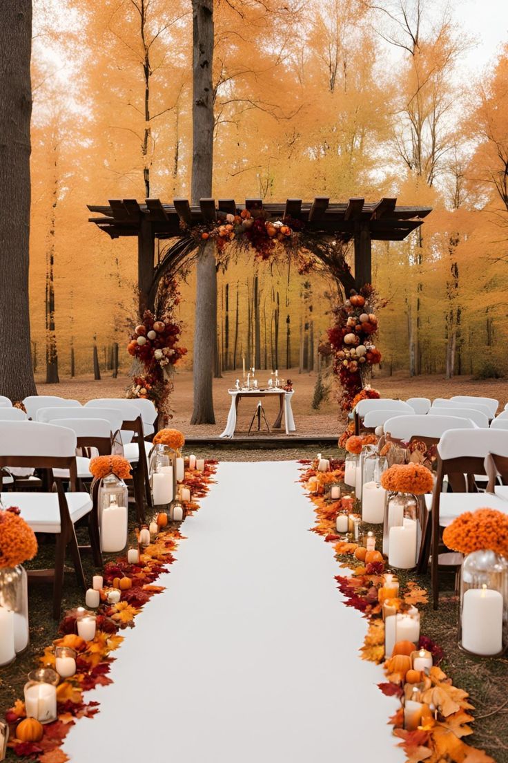 an outdoor ceremony set up with candles and pumpkins on the aisle, surrounded by fall foliage