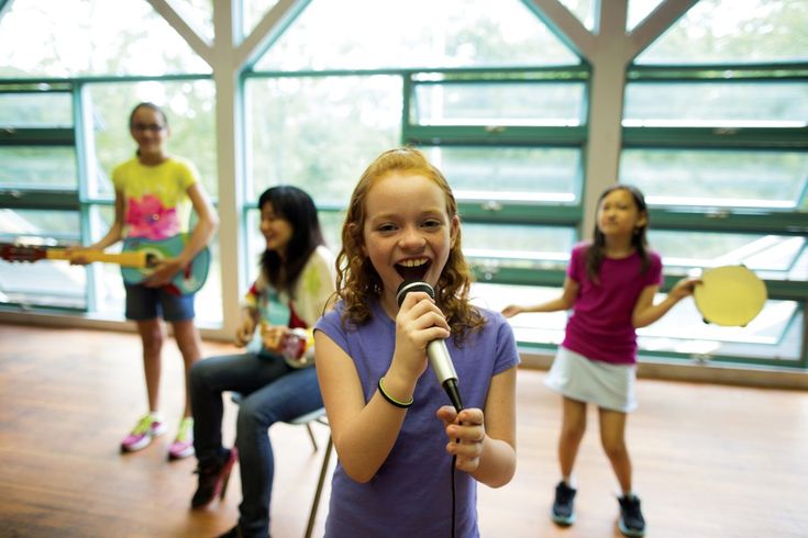 a girl singing into a microphone with other girls in the background