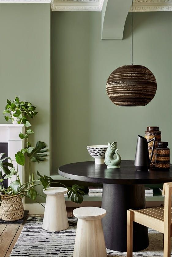 a dining room with green walls and wooden flooring is pictured in this image, there are several chairs around the table