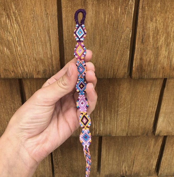 a hand holding a beaded bracelet on top of a wooden floor next to a wall