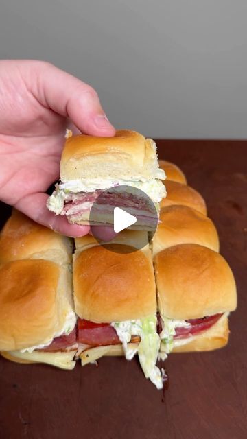 a person holding a sandwich cut in half on top of a wooden table next to a knife