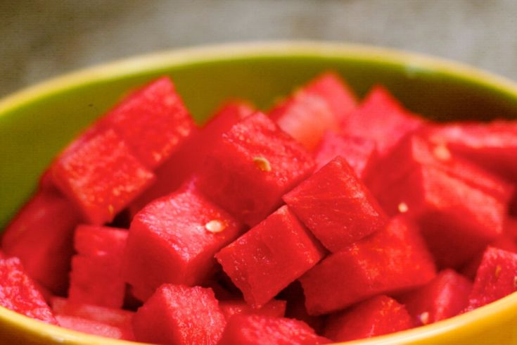 a yellow bowl filled with watermelon cut into cubes and sitting on top of a table