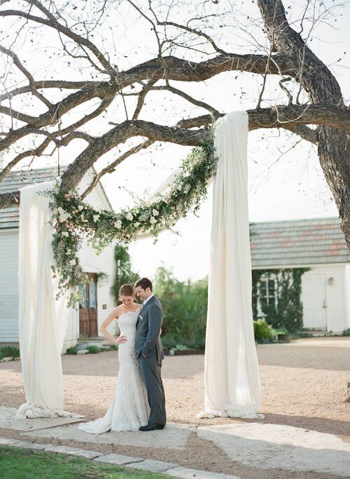 a bride and groom standing under an outdoor wedding ceremony arch with white draping