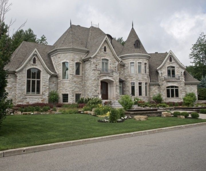 a large stone house sitting on the side of a road next to a lush green field